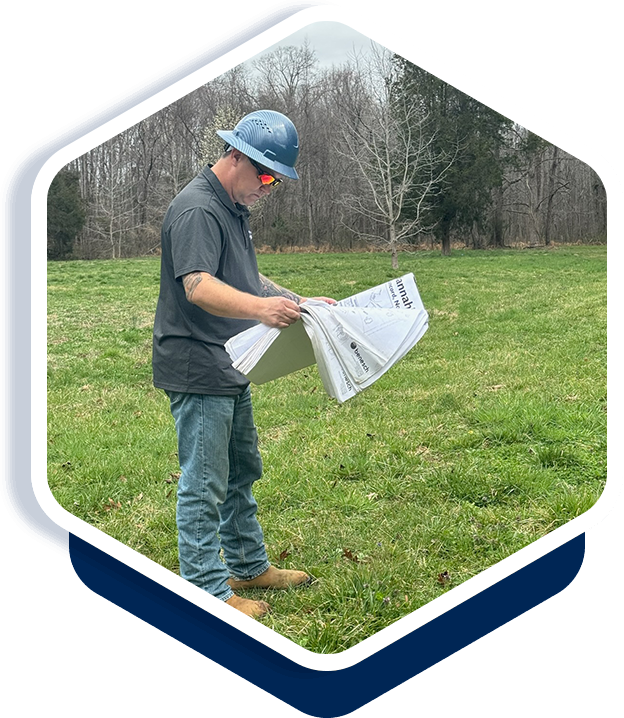 A man in a field holding papers and looking at them.